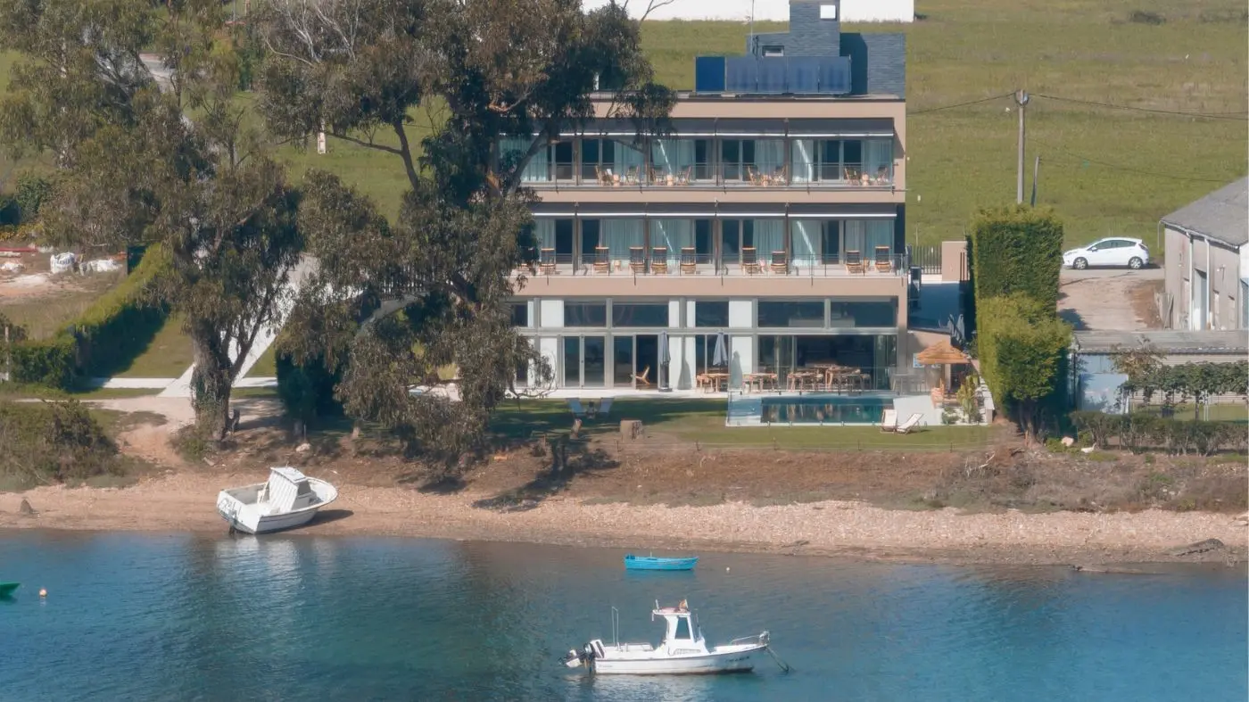 Hotel en Foz Malates visto desde la ría de Foz, con el edificio junto al agua y una barca